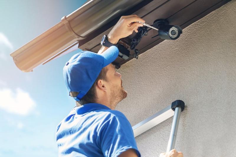 Installer mounting a wired security camera under a roof edge